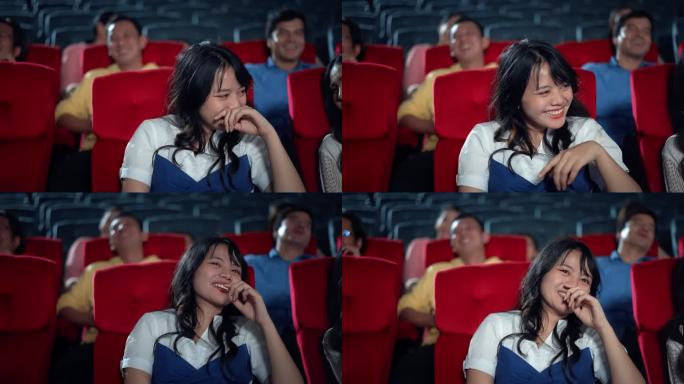年轻的亚洲妇女笑着享受在电影院看电影。