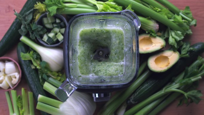自上而下的搅拌机动作捕捉绿色排毒果汁准备慢动作，芹菜，鳄梨，茴香和黄瓜