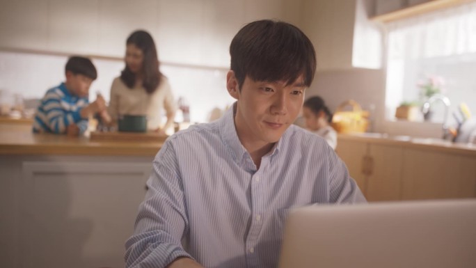 韩国家庭的延时摄影:年轻的父亲使用笔记本电脑远程工作，他的妻子和孩子在后台准备午餐。支持一个商人的家