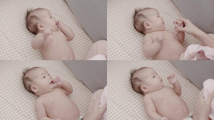 亚洲新生婴儿被母亲盖在床单上穿衣服。父母用爱照顾他们的孩子。