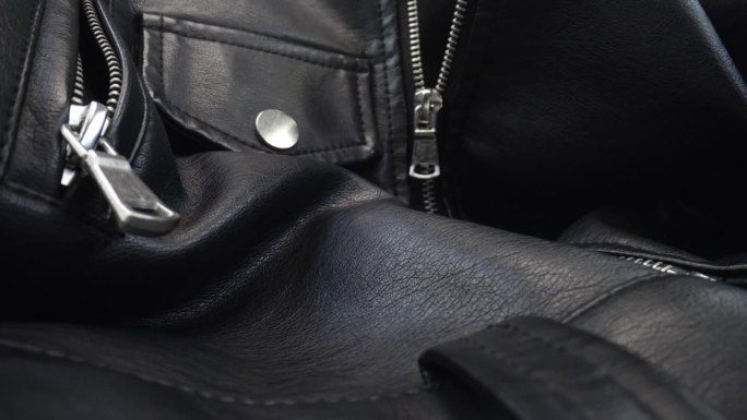 微距拍摄黑色皮夹克服装材质。滑块小车皮革纹理，相机滑过纹理织物和银色拉链