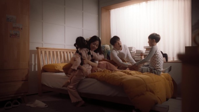 幸福的韩国家庭在早上:活跃和顽皮的孩子跑到他们的父母的卧室叫醒他们。兴奋的孩子强迫他们的父母下床一起
