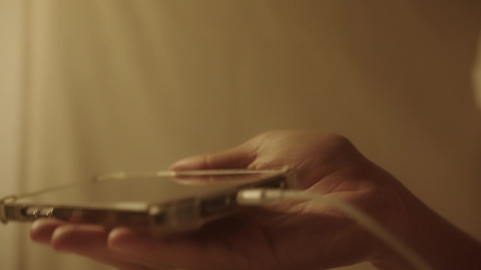 一个男人在晚上用手给智能手机插充电线的特写。