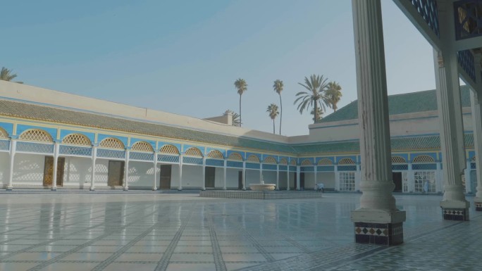 漫步在摩洛哥马拉喀什巴伊亚宫装饰精美的墙壁内的圆柱上，古老的马赛克墙壁，石头地板和蓝色的天空