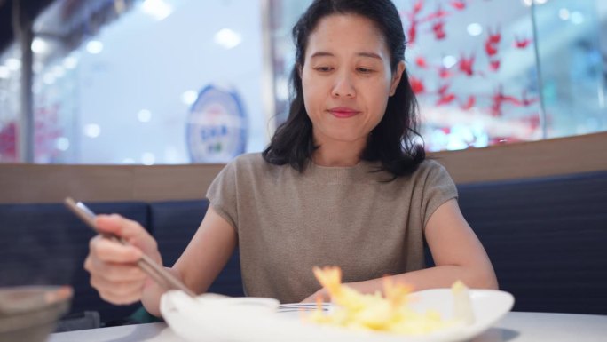 亚洲妇女完全沉浸在品尝油炸虾的烹饪之旅中。用筷子，熟练地夹起一只多汁的虾，送进嘴里。日本的饮食文化和