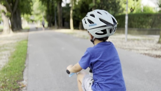 小男孩在公园骑自行车白天戴着头盔，仍然获得信心-失去平衡和焦点时，一群骑自行车的人超过