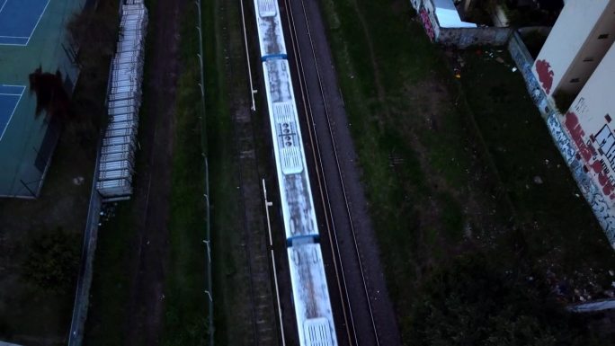 城市火车在铁路上行动在黄昏，傍晚，无人机的顶部视图
