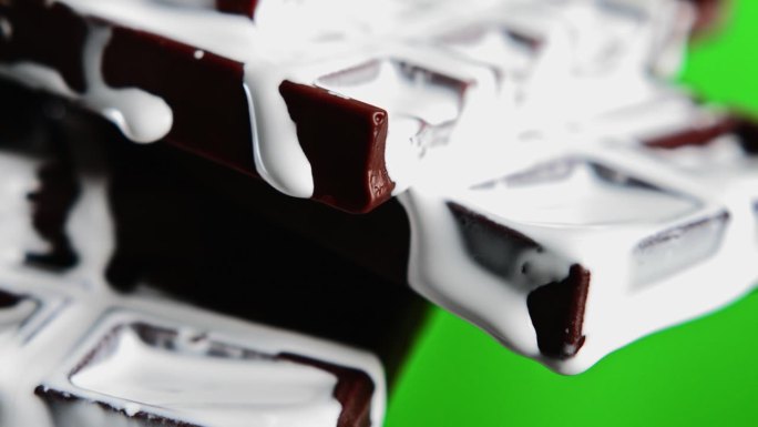 对比鲜明的黑巧克力棒和飘洒的甜白巧克力釉的特写。股票剪辑。美味的巧克力在绿色色度键的背景。