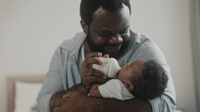 一位非洲父亲在家里把奶瓶里的牛奶拿出来喂他的小男婴。