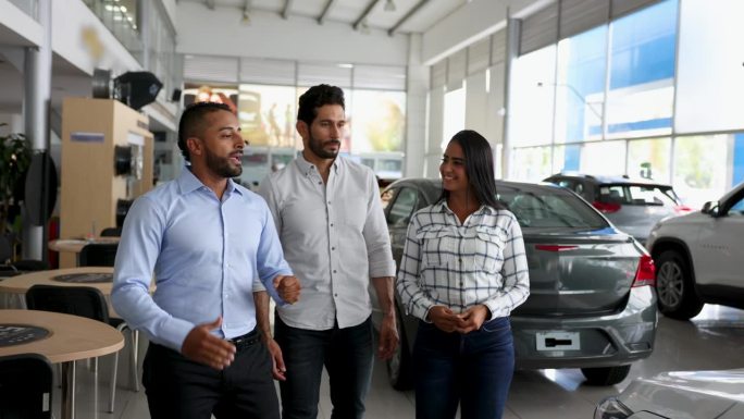 一个兴高采烈的推销员和一对幸福的夫妇在汽车经销店边走边谈论他要给他们看的一辆车