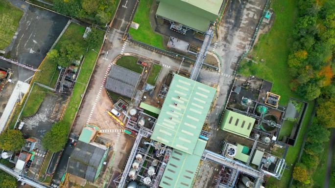 航拍镜头放大了英国一家工业化工厂，突出了管道、金属结构、冷却塔和化学品储存。