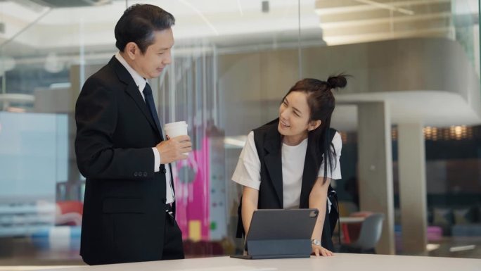 商人男女在办公室里见面聊天。一名亚洲男子端着咖啡杯，看着桌上的笔记本电脑。
