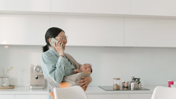亚洲妈妈带着襁褓中的婴儿在智能手机上聊天