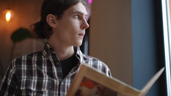 一个聪明的年轻人看着窗外看书的慢镜头。一个自信的白人坐在咖啡馆里等着点餐。