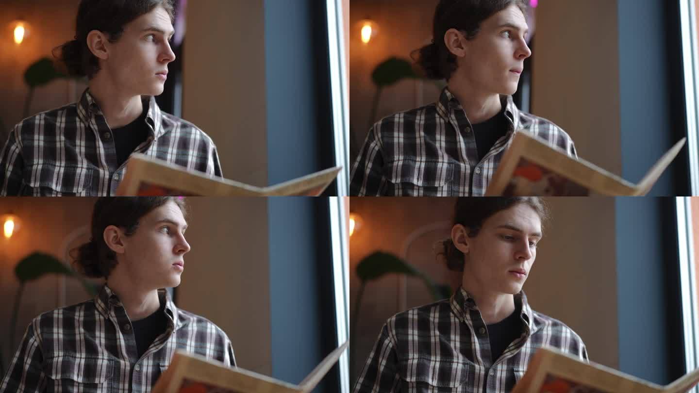 一个聪明的年轻人看着窗外看书的慢镜头。一个自信的白人坐在咖啡馆里等着点餐。