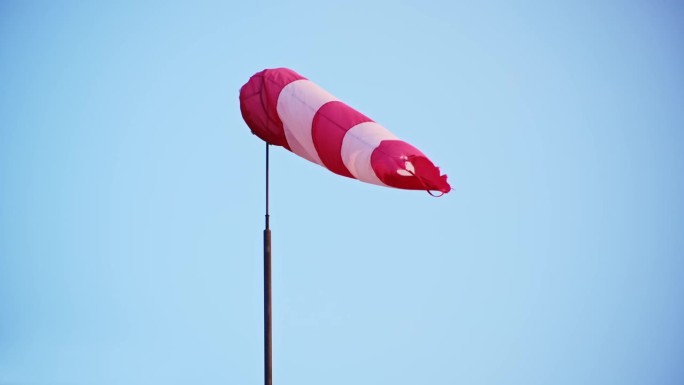安装在通航机场大楼楼顶的红白条纹风袜风锥风套指示器，向驾驶飞机的飞行员显示风速和风向
