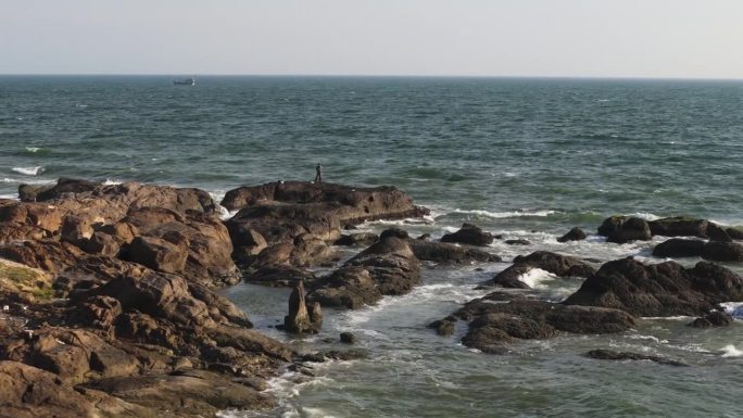 在越南美奈，无人驾驶飞机环绕着一名独自冲浪的男子。戏剧性的海浪冲击着岩石海岸。