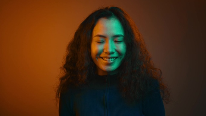 霓虹灯下亚洲年轻女子对着镜头微笑的快乐肖像。近距离观察迷人的人与白色的牙齿咧嘴笑。俏皮的20多岁女孩