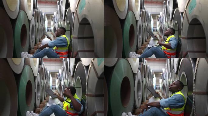 一个年轻人在仓库里储存金属片材料卷。坐下来休息一下，擦去汗水，然后继续工作。