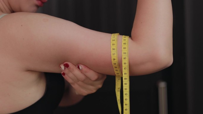 特写，一个女人抓着多余脂肪的上臂。捏紧松弛下垂的肌肉。女性饮食生活理念。
