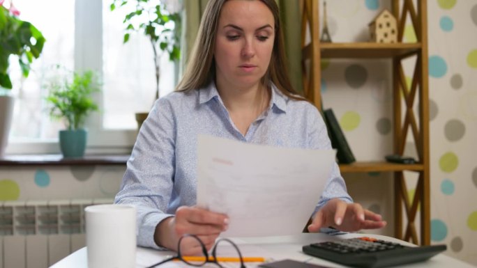 疲惫沮丧的女人坐在办公桌前拿着纸质账单，为银行贷款支付感到压力，担心未付的税款和财务问题