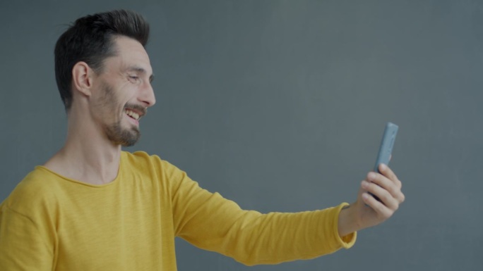 一名年轻人正在用智能手机进行在线视频通话，在灰色背景上竖起大拇指
