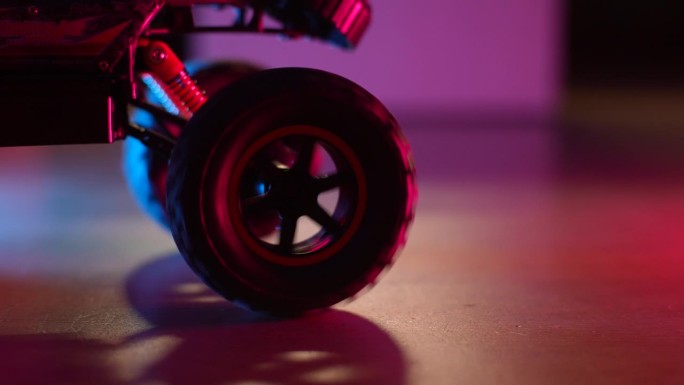 在霓虹灯的背景下，在黑暗的客厅里，遥控玩具车在地板上行驶、拖拉、旋转的特写。儿童玩具的概念。