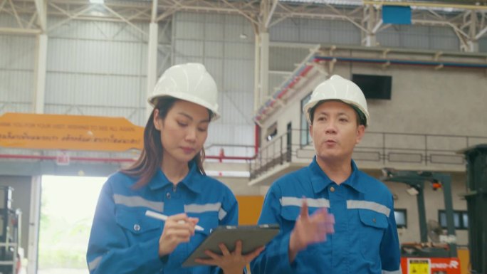 年轻的亚洲女工和男经理在制造厂边走边用平板查库存，边谈边聊。在制造厂或生产厂工作。
