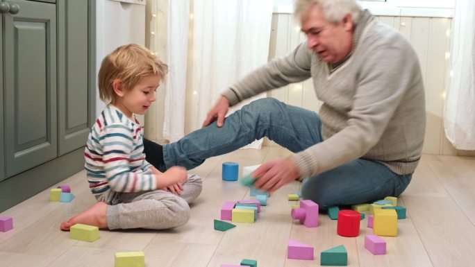 老爷爷和小男孩在地板上玩积木。两代同堂。老人和小孩玩得开心，在家里建塔笑。与爷爷共度快乐时光