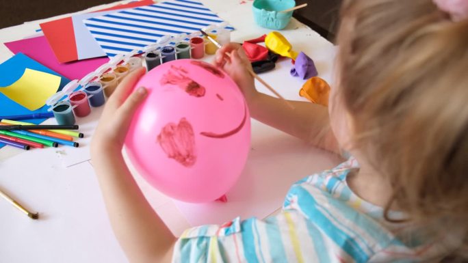 小女孩在气球上画着滑稽的笑脸。可爱的玩具，母亲节，生日或情人节。工艺美术概念。学习，教育，想象力