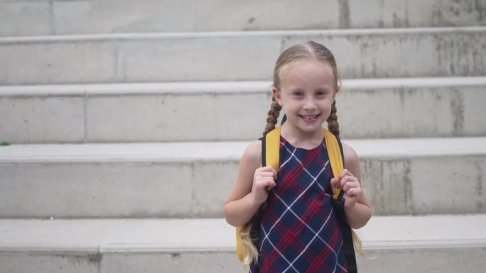 穿着格子裙背着书包的小女孩微笑着站在石阶旁，小女孩背着书包