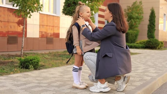 妈妈陪着她一年级的女儿去学校，亲吻她，拥抱她，回到学校，家长把孩子送到一年级。妈妈遇到了学校里的一个