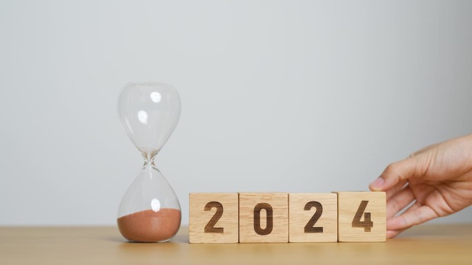 2024文本与沙漏在桌子上。决心，时间，计划，目标，动力，重启，倒计时和新年假期的概念