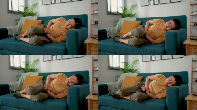 一位亚洲妇女胃痛得躺在家里客厅的沙发上。
