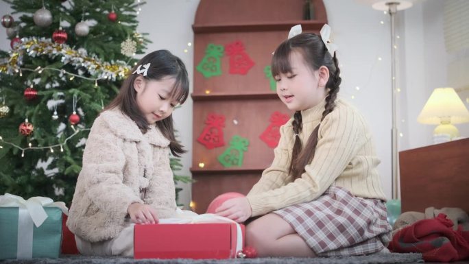 两个快乐的兄弟姐妹坐在美丽的节日客厅的地板上打开圣诞礼盒