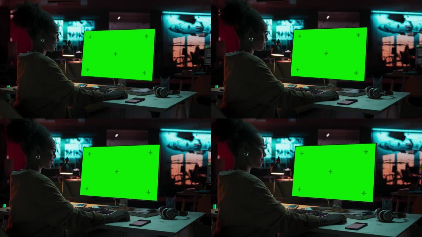 富有创造力的黑人女性坐在她的办公桌前使用桌面电脑的肖像与绿屏模型。在游戏开发初创公司工作的女性专家，