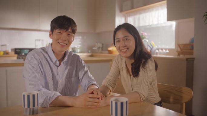慢镜头吸引韩国年轻夫妇坐在家里聊天。男女朋友在厨房里谈笑风生。健康生活方式的家庭，对着相机微笑