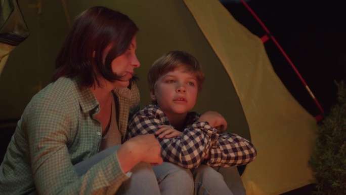 妈妈和孩子在篝火边聊天。家庭露营夜聊。