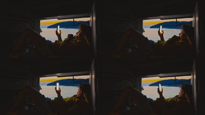 一名男子斜倚在露营车上的床上玩智能手机