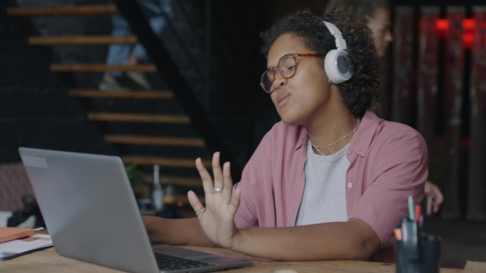 快乐的非裔美国商务女性在联合办公办公室用笔记本电脑工作，戴着耳机听音乐