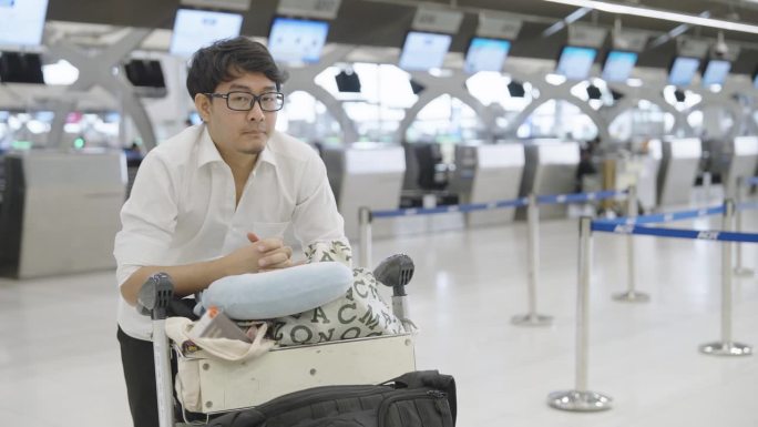 一名亚洲男子拿着行李在机场候机柜台打呵欠