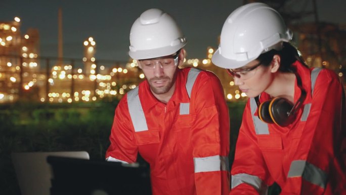 两名检查工程师在夜间使用炼油厂和炼油厂的笔记本电脑检查工厂的生产质量，能源生产的研发理念