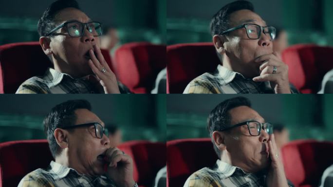 震惊的亚洲成熟男子在电影院看恐怖电影。