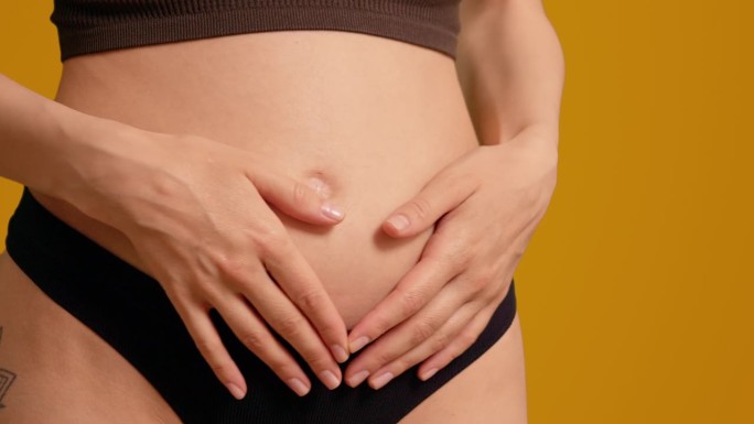 穿着黑色内裤的孕妇在橙色屏幕背景上摸着肚子。