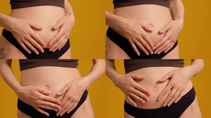 穿着黑色内裤的孕妇在橙色屏幕背景上摸着肚子。
