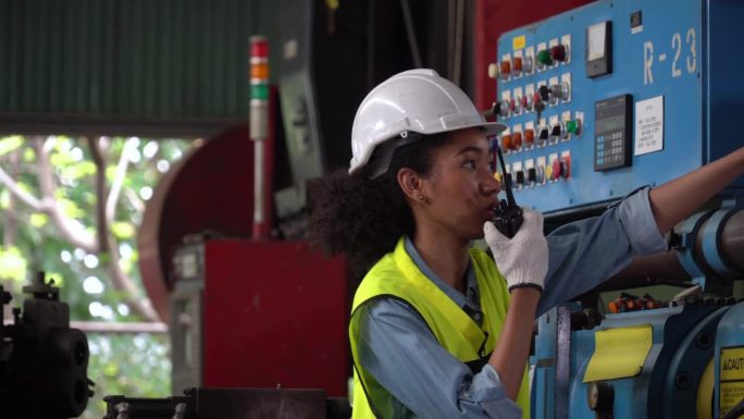非裔美国人女工业工程师在工业工厂检查控制柜机器。检查或操作重型机械的黑人女性机械技师对着收音机讲话