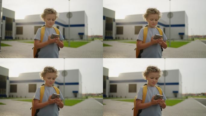 小男孩在课间休息时使用智能手机的照片，站在校园里
