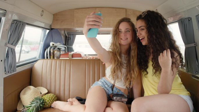 漂亮的好朋友在复古的露营车里用智能手机自拍，复古风格的社交媒体微笑着玩得开心
