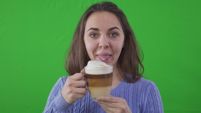 特写咔哒咔哒的隔板和白人美女喝咖啡看着镜头。前视图肖像自信迷人的女演员广告卡布奇诺在绿屏背景。