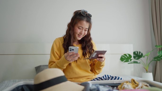 快乐的年轻亚洲女子在智能手机上网上购票，准备旅行。女性在旅行前用智能手机预订酒店或航班。旅游的概念